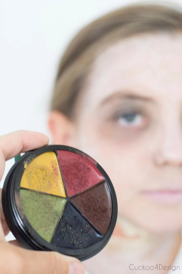 extreme close up of a paint palette, with yellow and red, green and black, and brown colors, scary face paint, child with a white face in the background