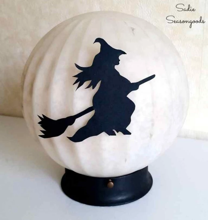cream colored round lamp, on a small black plastic stand, decorated with a black cutout, shaped like a witch on a broom, halloween witch decorations, diy moon lamp