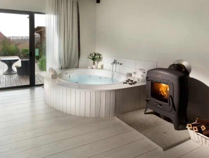 heater powered by wood, inside a room, with a light laminate floor, containing a hot tub, lined with white wood, master bath remodel, large window overlooking a garden