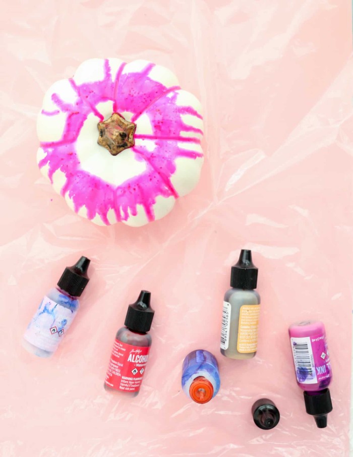 fuchsia pink paint, running down a small, fake white pumpkin, halloween pumpkin decorations, five small bottles, of liquid paint in different colors