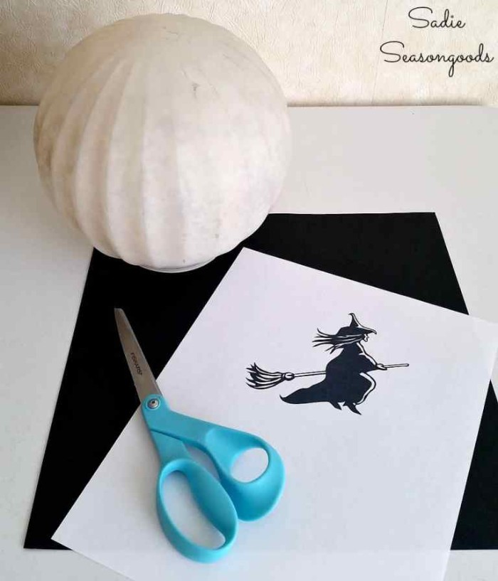 spherical white lamp, a sheet of black card, a pair of scissors, and a white piece of paper, with a simple drawing of a witch, in black and white, materials needed for making, halloween witch decorations