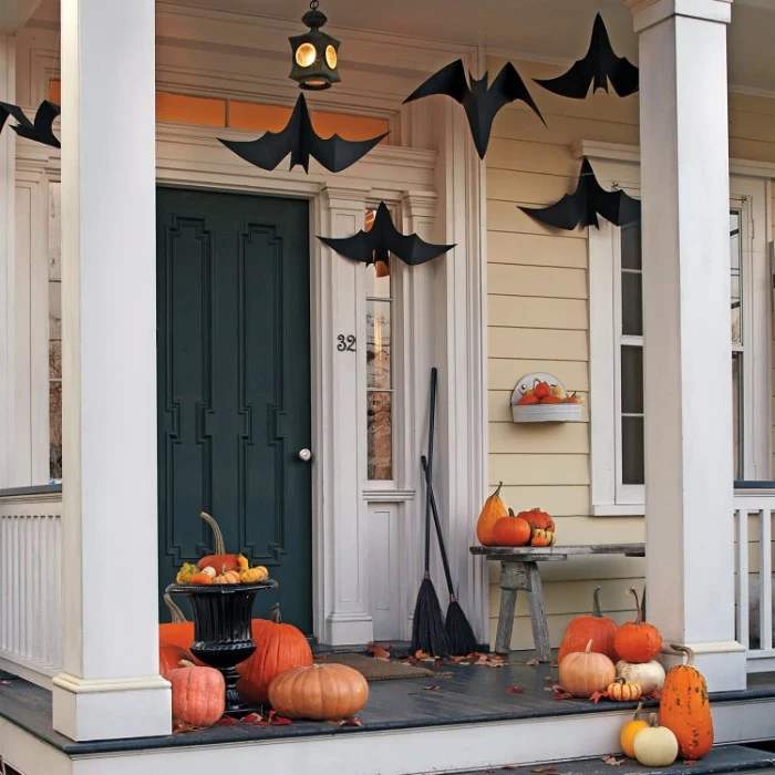 porch decorated with several pumpkins, in different shapes and sizes, halloween pumpkin decorations, black paper bats, hanging above them