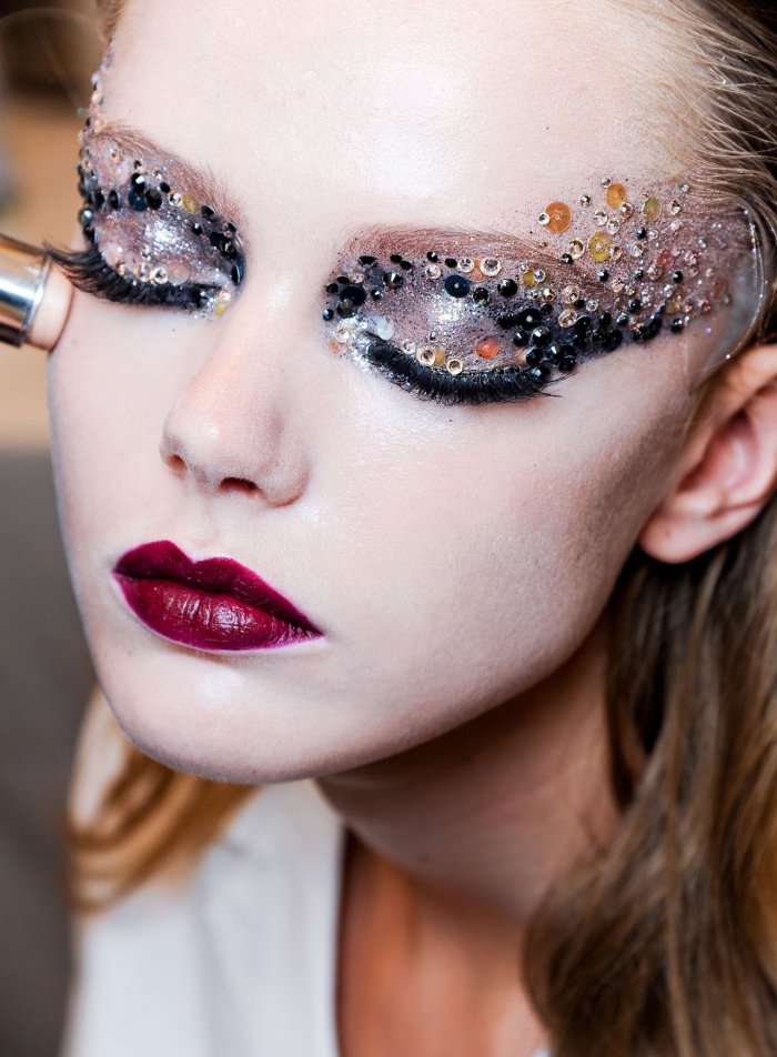 small beads in black, and silver and gold sequins, decorating the eyelids of a pale young woman, christmas eye makeup, with dark red lipstick, and silver eye shadow