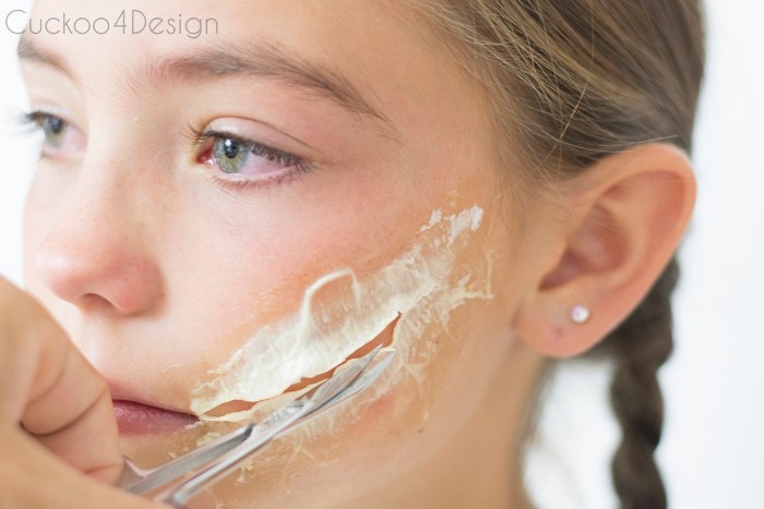 hand holding a small pair of scissors, and cutting dried special effects makeup wax, stuck on the cheek of a young female child, scary face paint, zombie costume tutorial