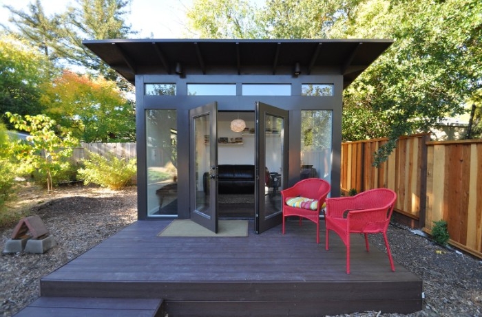 fuchsia pink garden chairs, placed on a dark grey wooden dock, near a modern shed, with open doors