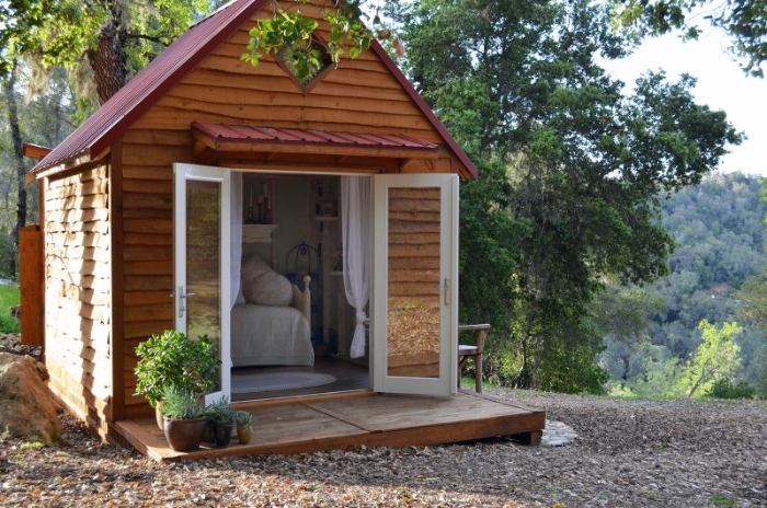 wooden shed ideas, small structure with open glass doors, built on a pebbled surface, and surrounded by trees