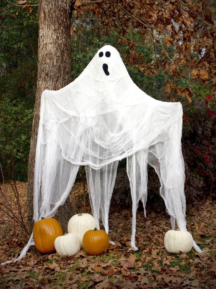 fall garden with fallen leaves, and several pumpkins, decorated with a ghost, made from sheer white fabric, with a simple, hand-painted face