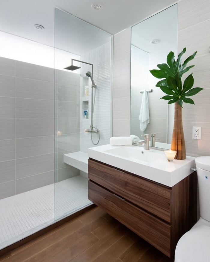 toilet seat in white, near a rectangular white sink, placed over a dark brown cupboard, master bathroom remodel, shower cabin with a glass divider
