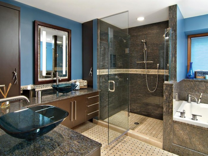 open door of a glass shower cabin, inside a bathroom, with blue and grey walls, beige tiled floor, and brown cupboards