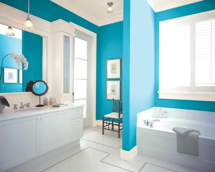 cerulean blue walls, with white plaster details, in a bright bathroom, with white furniture, best bathroom paint colors, white floor and a bathtub
