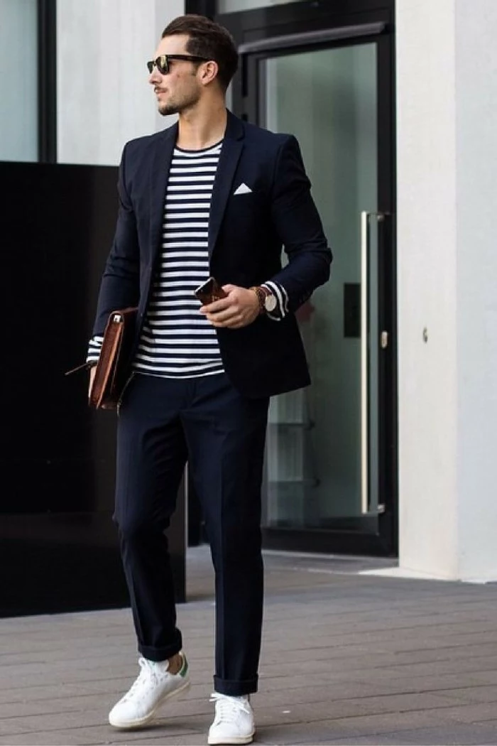 striped jumper in black and white, worn with a dark navy blazer, and matching smart, dark navy trousers, capsule wardrobe men, white sneakers and sunglasses