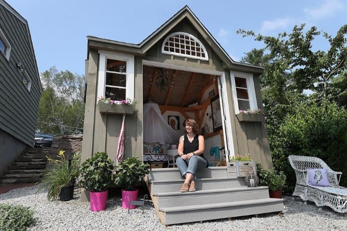 woman sitting on a small staircase, in front of a pale grey shed, with three windows, and open doors, shed ideas, furniture visible inside