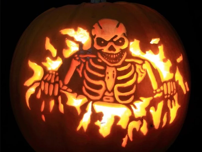 evil laughing skeletton, carved on an orange pumpkin, lit with candles from within, skeleton pumpkin, in a dark space