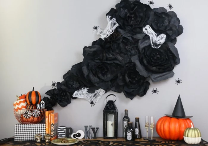 wall decoration made from black, white and grey fabric, made to look like smoke, haunted house decorations, surrounded by black plastic spiders, near a shelf with candles, painted pumpkins and other ornaments
