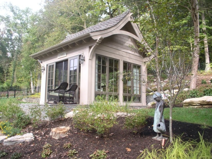 classic garden shed, with large windows, a gabled roof, and open doors, surrounded by trees, with a statue of a little girl nearby