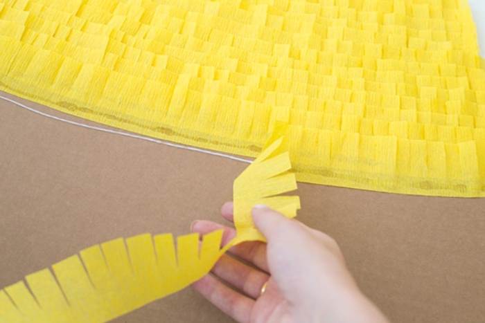 layers upon leyars, of frayed strips of yellow tissue paper, stuck on a piece of beige cardboard, couples halloween costumes, hand holding more yellow paper nearby