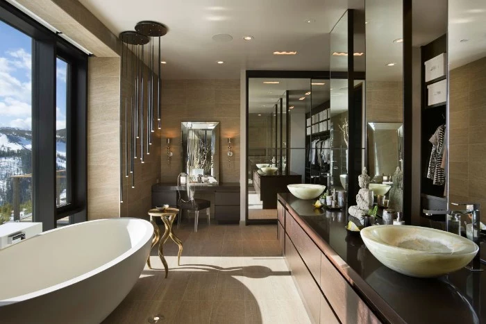 mirrored surfaces inside a large bathroom, with an oval white bathtub, dark brown cupboards, and ivory-colored sinks