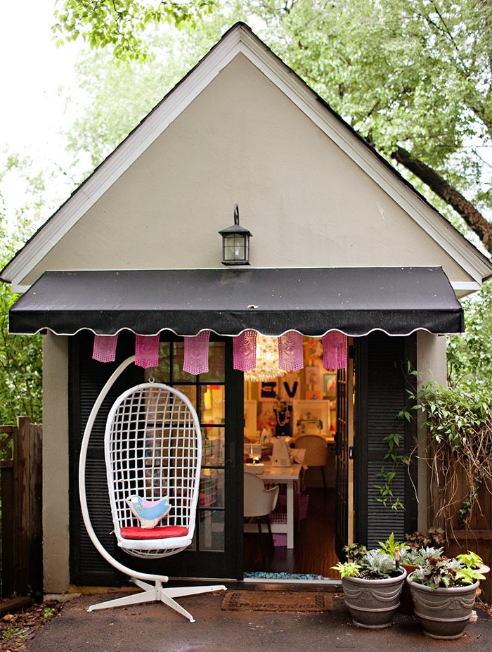 gabled roof on a small house, in off white and dark grey, several pots with plants, and a swing chair, shed ideas