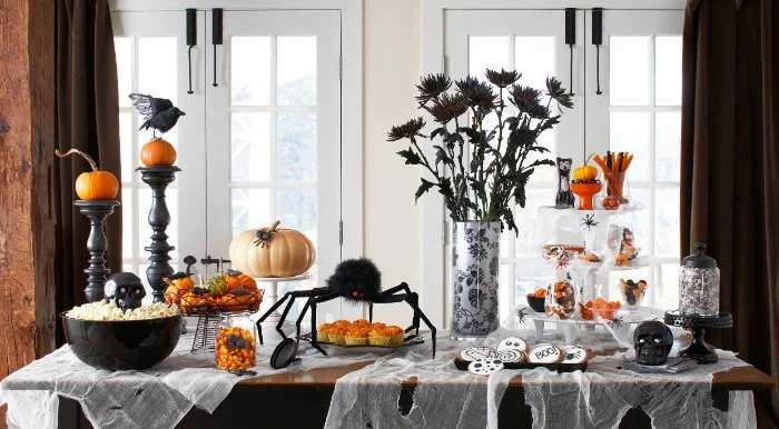 flowers in black, in a vase, on a table, covered in fake cobwebs, with a big black spider ornament, black candlesticks, pumpkins and different snacks, haunted house decorations 