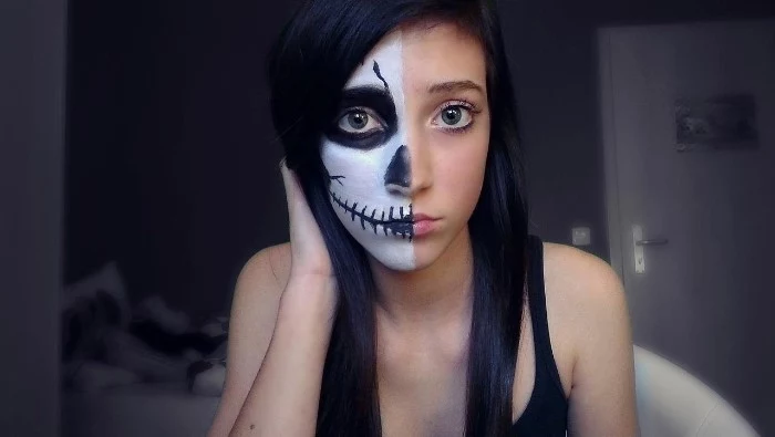 slim young girl, dressed in a black tank top, half of her face is painted to look like a skull, while the other half is left bare