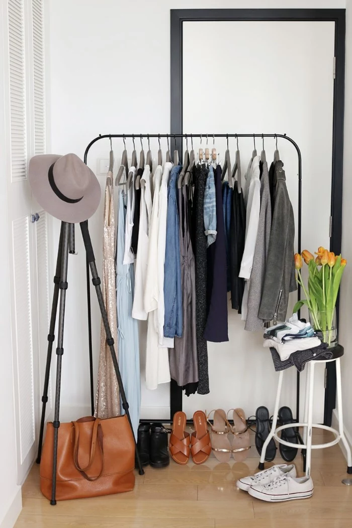capsule wardrobe, black metal clothes rack, with several outfits on hangers, five pairs of shoes, a brown leather bag, and a grey hat