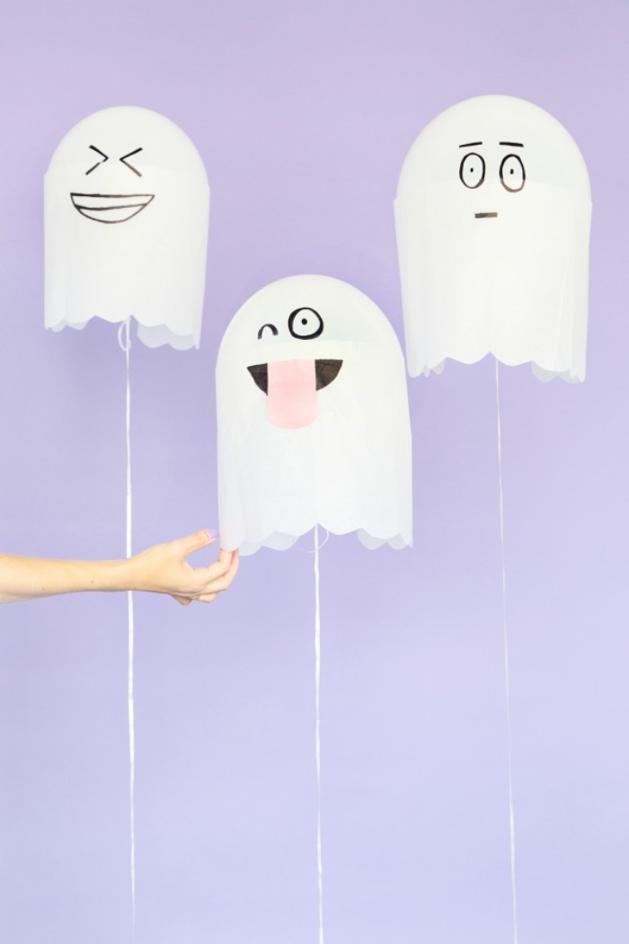 balloons in white, decorated with paper, to look like ghosts, with funny hand-painted faces, halloween party decoration ideas, hand holding one of the balloons 
