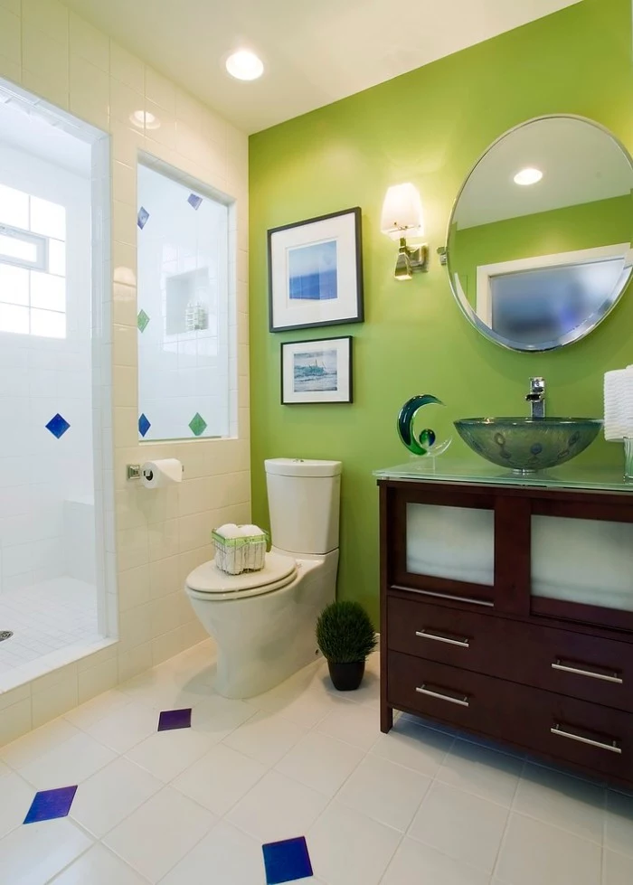 bathroom accent wall in lime green, inside a room covered in white tiles, with blue details, dark brown cupboard with a sink, toilet and two framed images