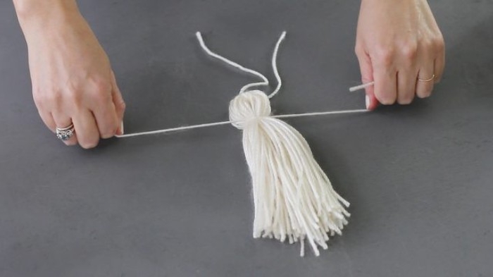 tassel made from white yarn, tied by two hands, on a dark grey background, room makeover idea, using arts and crafts