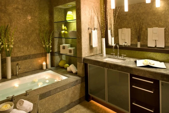 green and brown tiles, decorating the walls, of a bathroom, with an elevated bath, filled with water, and containing several floating lit candles