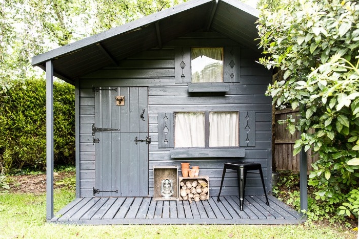 hut in the forest, made of dark grey wood, with two windows and one door, rustic she shed idea