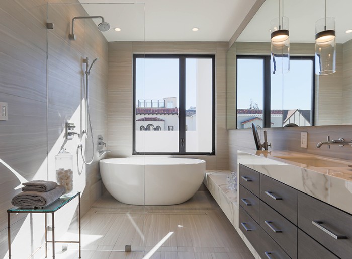 long rectangular mirror, decorating the wall of a btahroom, with a white oval bathtub, a shower area, and dark brown cupboards, with marble counter tops