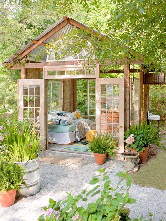 bright orangery style shed, made of wood and glass, she shed ideas, doors opened to reveal a sofa, with lots of cushions inside