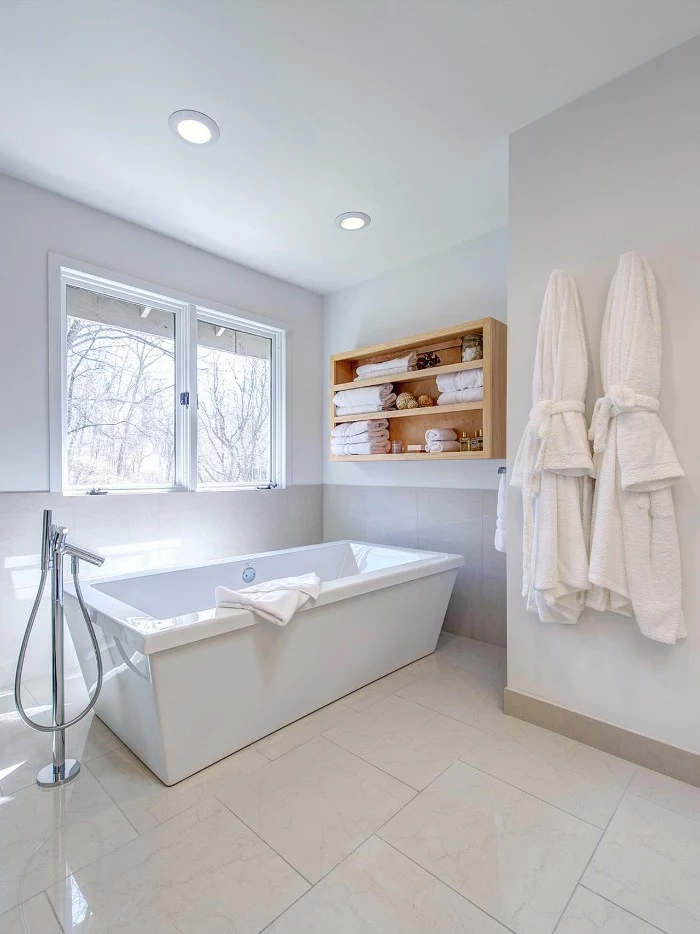 rectangular bathtub in white, inside a bright room, with a window, and pale beige floor, master bath remodel, two white bathrobes