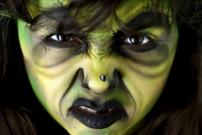 angry looking woman, with witch face paint, in green and yellow and black, wrinkles and large eyebrows, a fake black mole