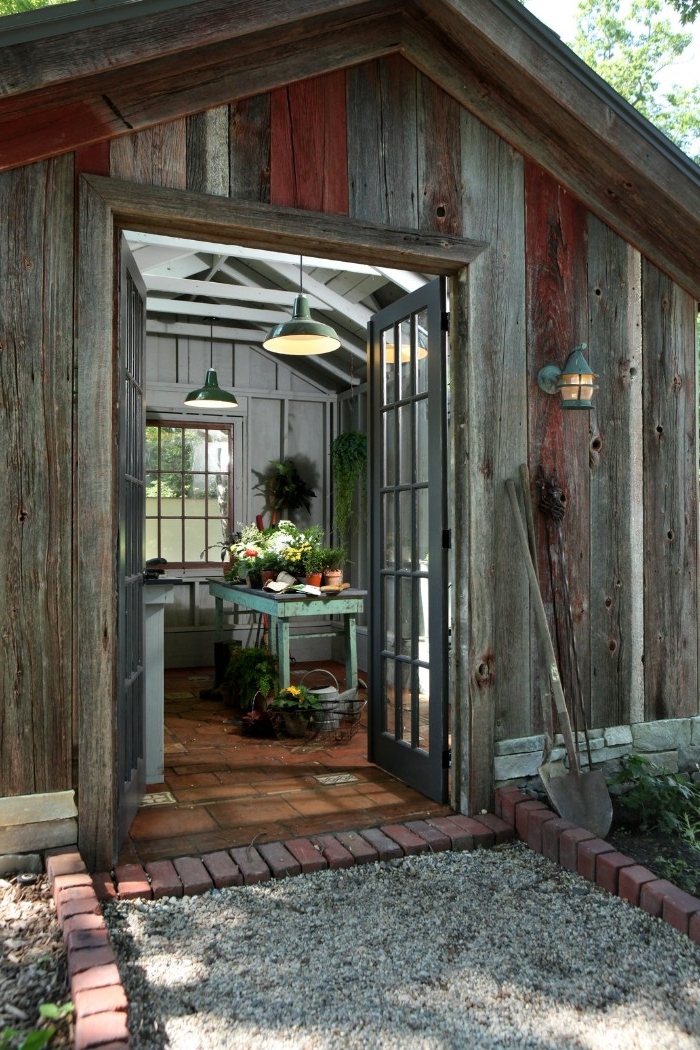 grey and brown wooden shed, with open double doors, revealing a vintage, duck's egg blue table, with flowers and potted plants, she shed