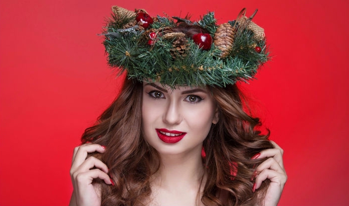 pine branches wreath, decorated with pinecones, and christmas ornaments, on the head of a brunette woman, with holiday makeup and wavy hair