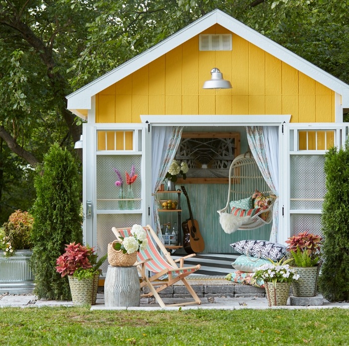 she shed in yellow and white, with open doors, revealing a swing, an acounstic guitar, and other items inside