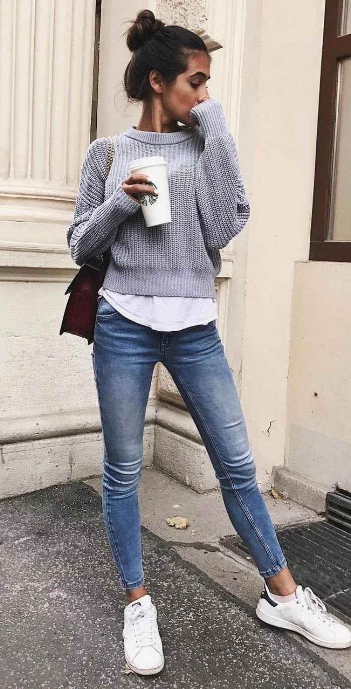 top knot worn by a brunette, slim young woman, dressed in blue skinny jeans, with a white shirt, and a pale grey sweater