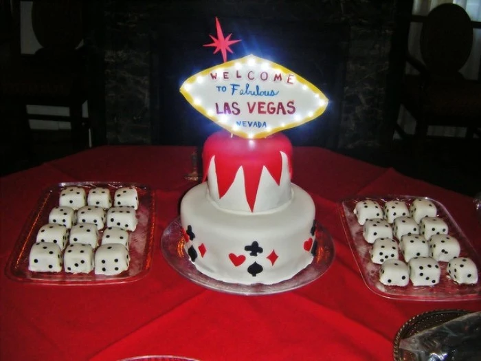 las vegas themed party, two glass trays filled with cube-shaped cakes, decorated to look like dice, birthday cake with glowing topper, shaped like the las vegas sign, 50th birthday party ideas for men