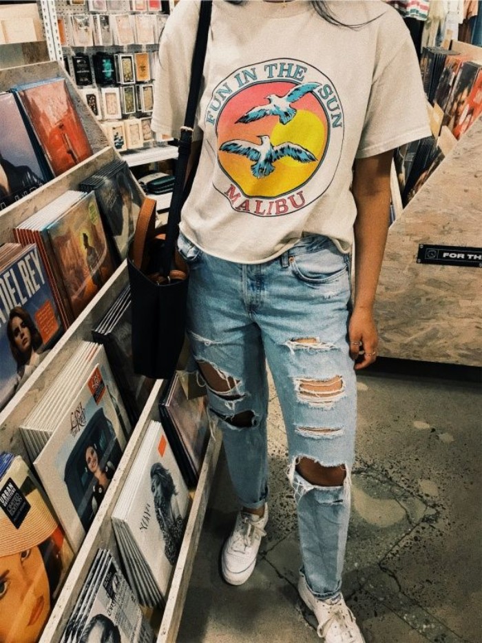 baggy white vintage t-shirt, with a colorful graphic print, worn with ripped, pale blue jeans, and white sneakers, by a girl standing in a record store
