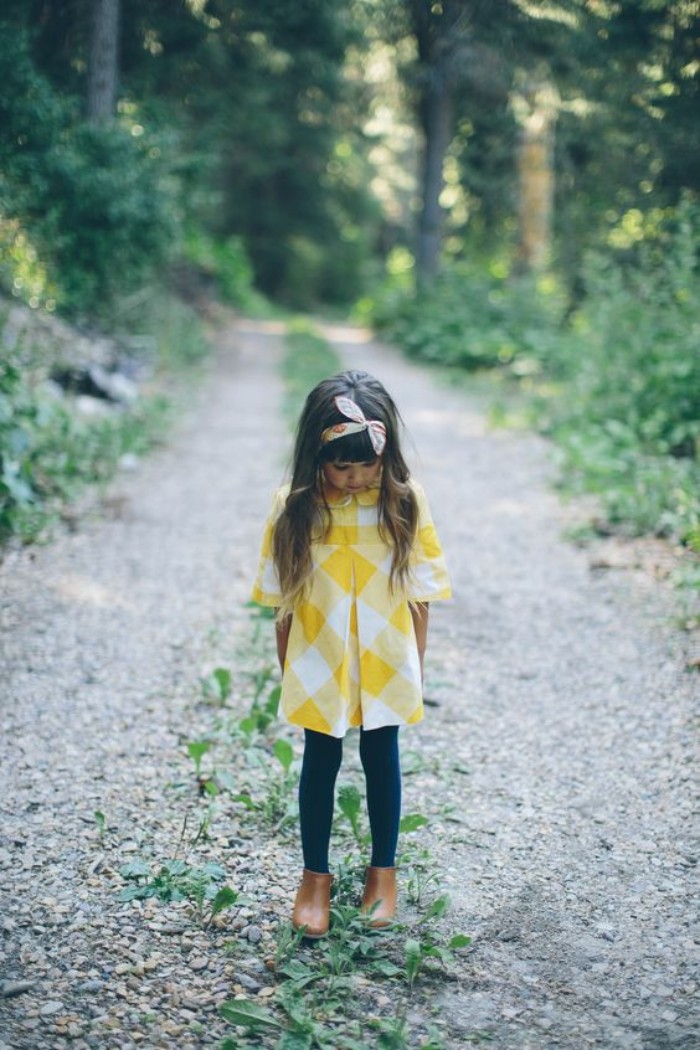 small girl dressed in a white and yellow, checkered tunic dress, over black leggings, toddler thanksgiving outfit, headband and brown ankle boots