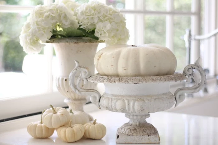 vases in antique style, with chipping white paint, one contains a white pumpkin, and the other - a bouquet of white hydrangeas, five small white pumpkins nearby