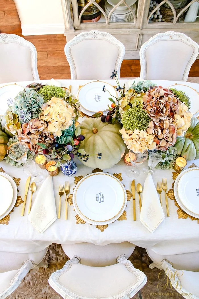 hydrangeas in different colors, accompanied by other plants, in two bouquets, placed on a table, set for a festive meal, cheap centerpiece ideas, pumpkins and lit candles, gold-rimmed plates and gold cutlery