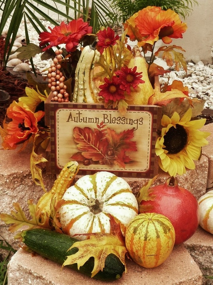 courgette and pomegranate, gourds and pumpkins, and faux flowers in red and orange, near a small wooden sign, decorated with fall leaves, and featuring the message autumn blessings