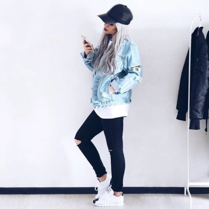 platinum blonde young woman, with long wavy hair, and a black baseball cap, holding a mobile phone, dressed in 90s grunge clothing, ripped black skinny jeans, white oversized t-shirt, and pale blue denim jacket, with a few patches 