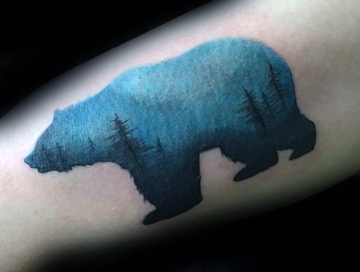 nature-inspired small tattoos with meaning, a bear-shaped watercolor-effect tattoo, decorated with multiple fir trees, in dark blue, on a light blue background