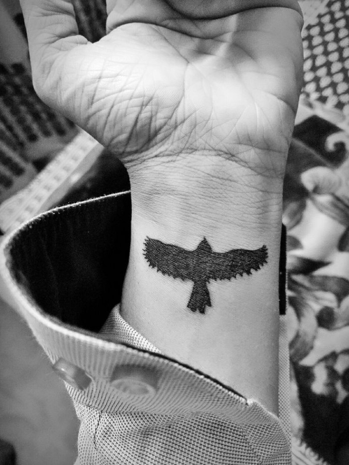 lower arm tattoos, a bird in flight, tattooed in solid black, on the wrist of a man, wearing a long sleeved shirt