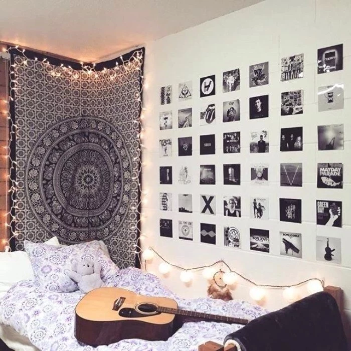 acoustic guitar laying on a bed, with white and blue bedding, teenage bedroom ideas for small rooms, walls decorated with black and white photos, and a fabric wall hanging, surrounded by lit fairy lights