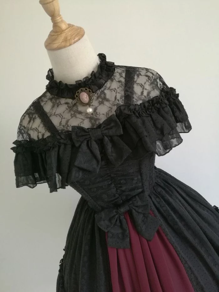 lolita style dress, made from black lace, with a purple detail, two bows and a cameo brooch, on a mannequin