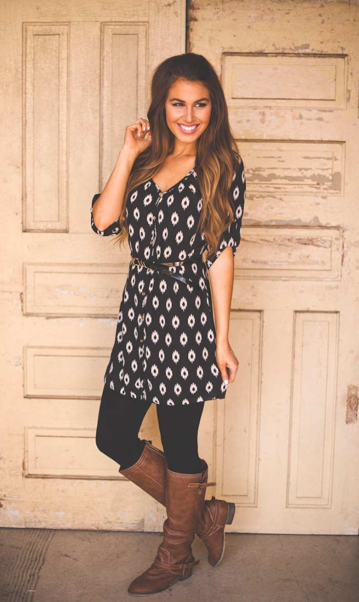 mini dress in black, with white geometrical pattern, worn over black leggings, by a smiling woman, with long brunette hair, and tall brown leather boots